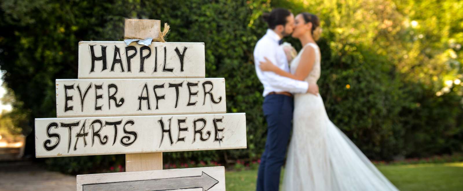 Bride and groom kissing outdoors next to wedding sign