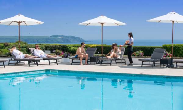 Outdoor pool with people being served drinks sea view