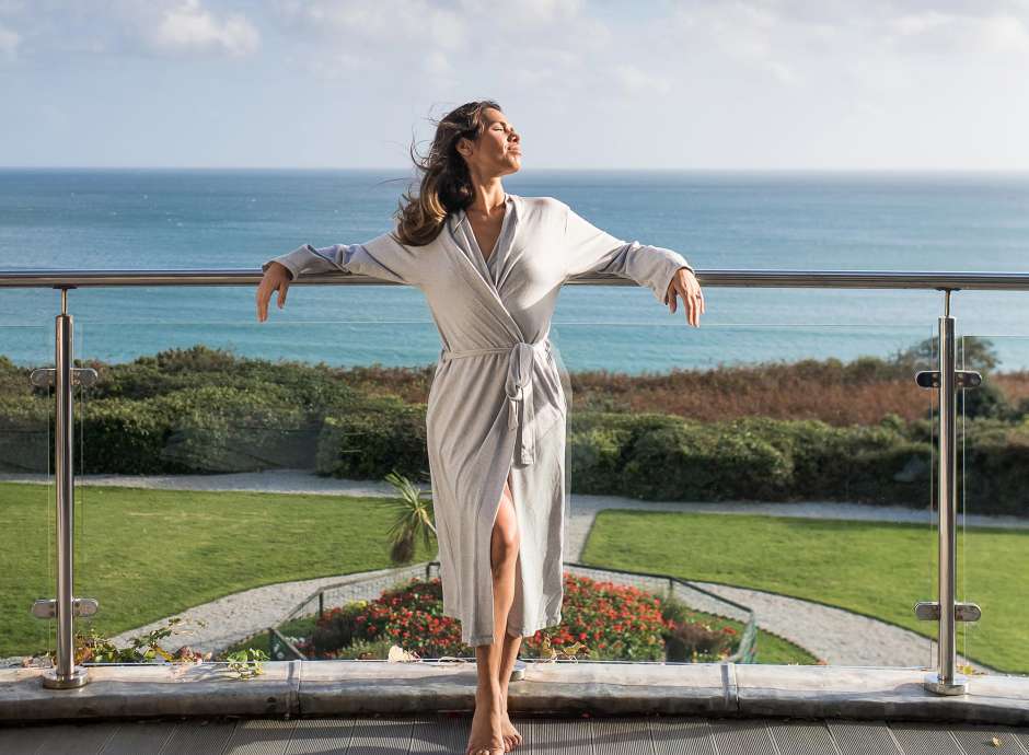 A woman wearing a dressing gown and relaxing on a balcony at the Carlyon Bay Hotel