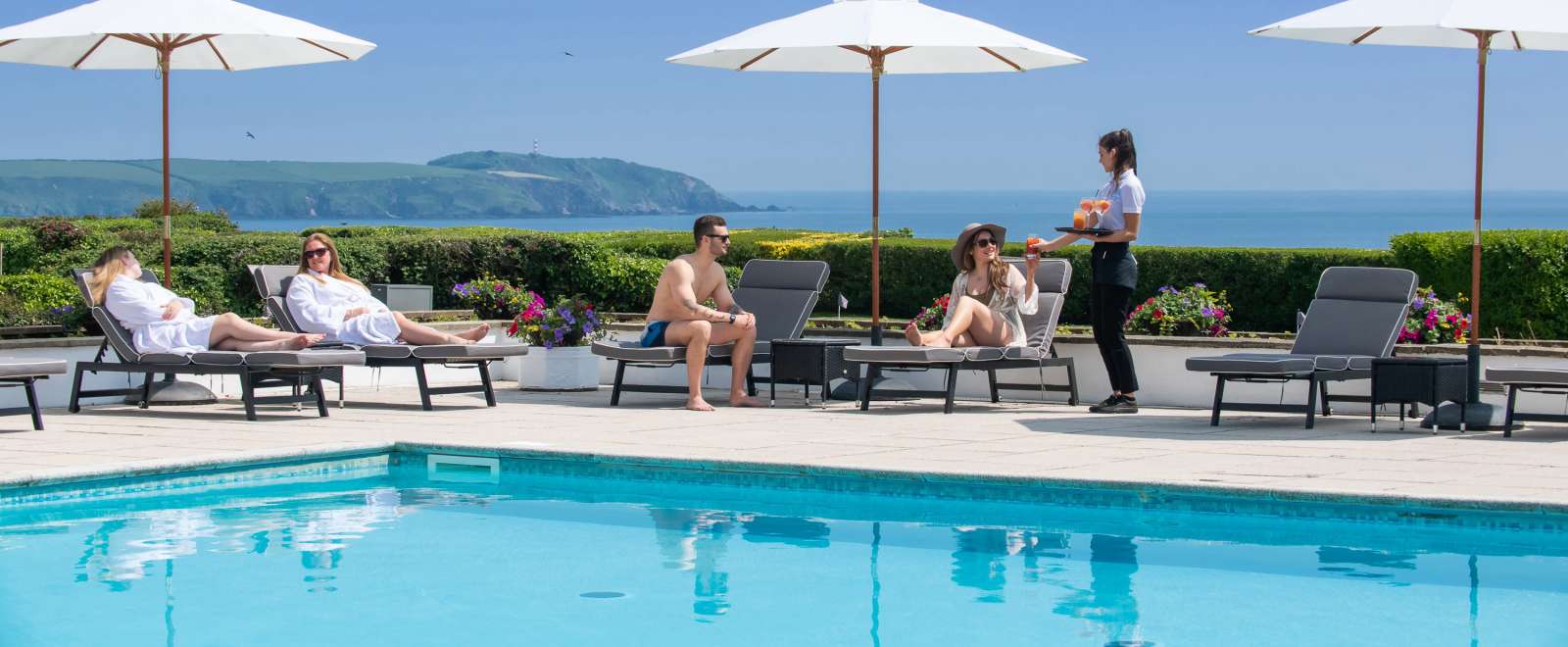 Outdoor pool with people being served drinks sea view