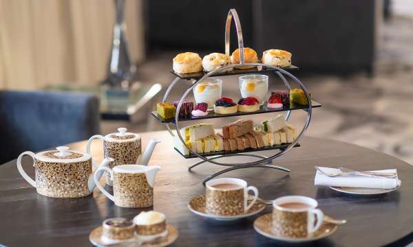 Afternoon tea rack on a table featuring scones, sandwiches and cakes with tea cups and tea pot