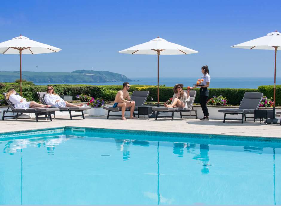 Outdoor pool with people being served drinks sea view